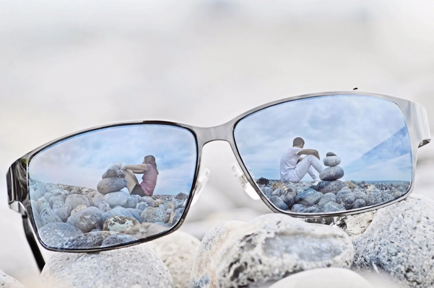Lunettes posées sur une plage de galets normande, montrant le reflet d'un couple